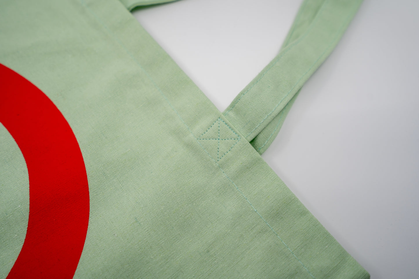 Stofftasche in Geiger-Grün mit einem großen roten „G“ auf der Vorder- und Rückseite und zwei Tragehenkeln.