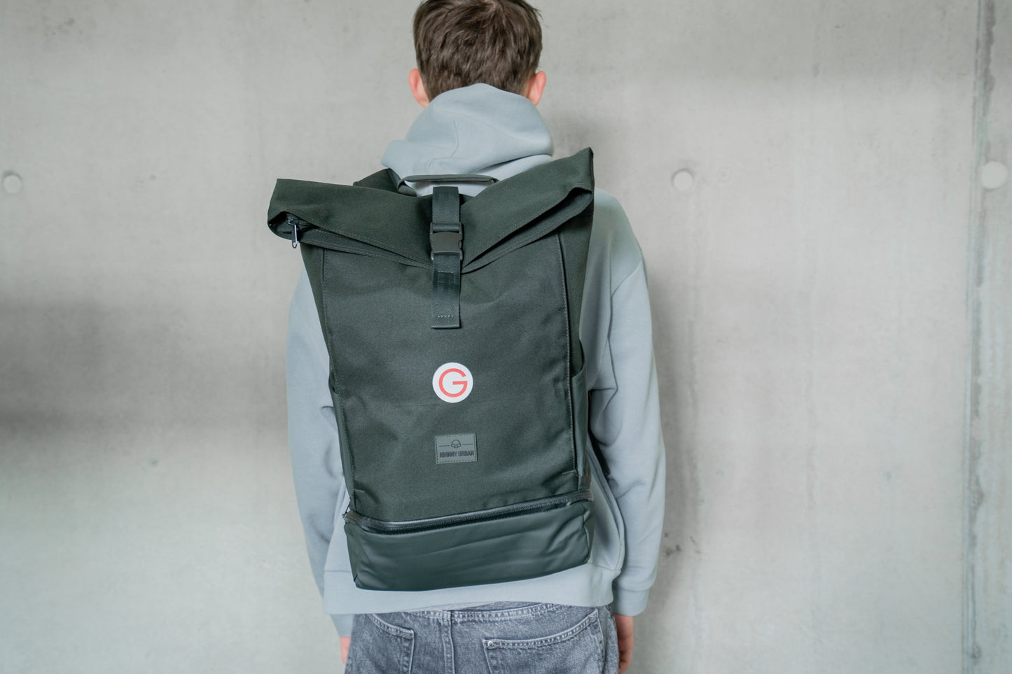Dunkelgrüner Rucksack mit kleinem, roten Geiger "G"mit Geiger-Grünem Hintergrund vorne.