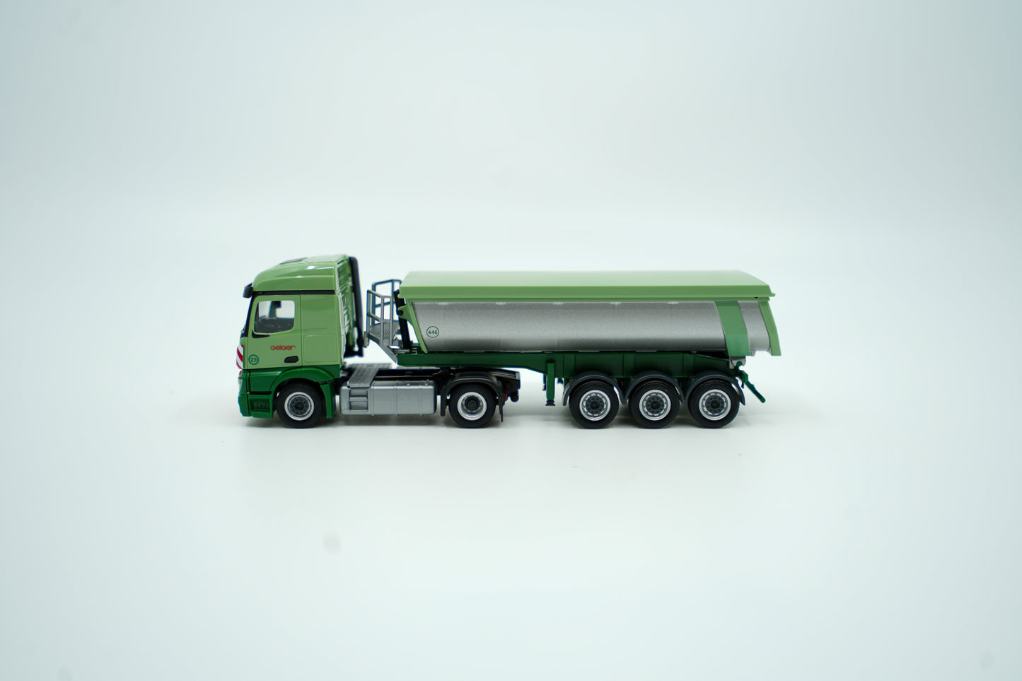 Miniaturmodell eines Mercedes Geiger-LKW in Geiger-Grün mit grauem Thermomulden Anhänger mit rotem "Geiger" Schriftzug. Verpackung inklusive.