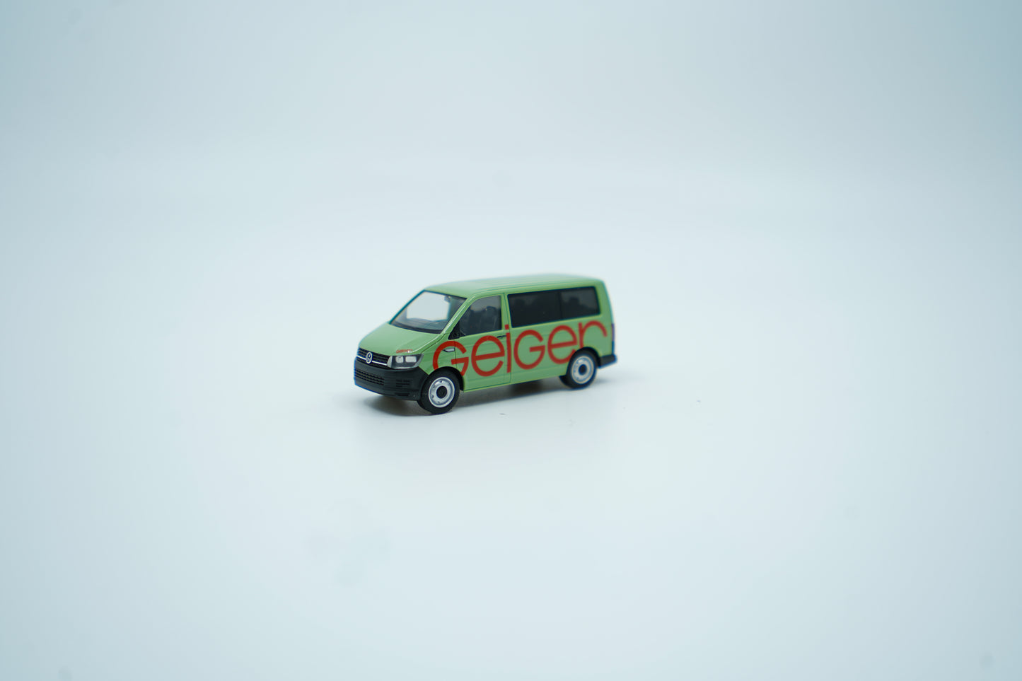 Miniaturmodell eines Geiger VW-Bus in Geiger-Grün mit rotem „Geiger“-Schriftzug, Verpackung inklusive.