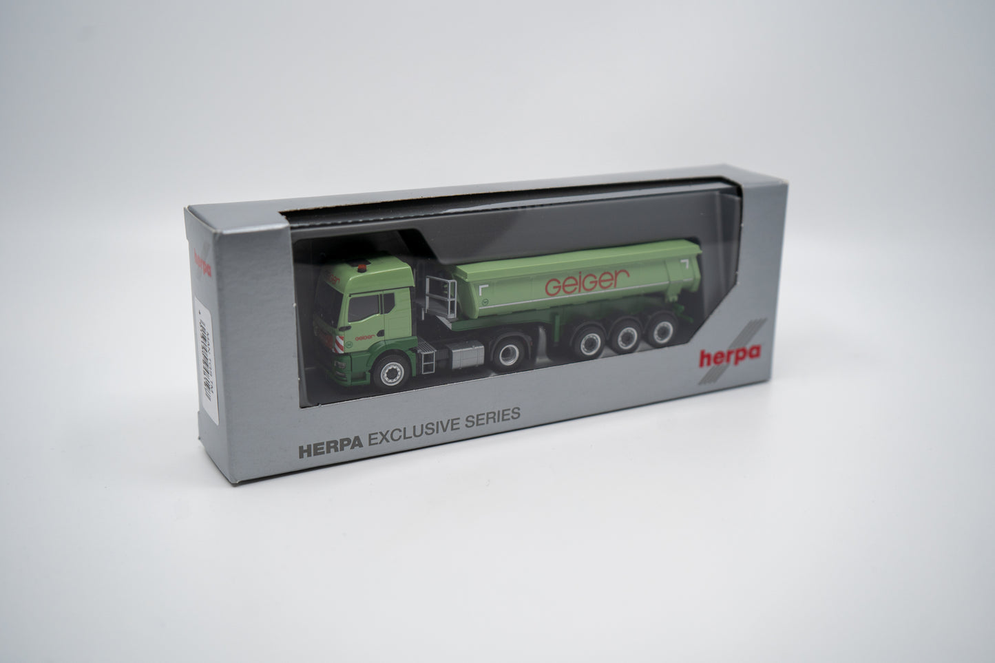 Miniaturmodell eines Mercedes Geiger-LKW in Geiger-Grün mit grauem Thermomulden Anhänger mit rotem "Geiger" Schriftzug. Verpackung inklusive.