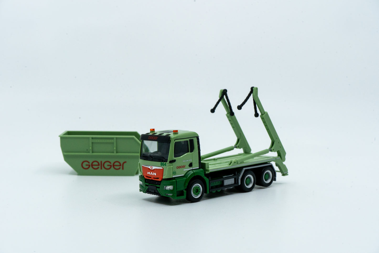 Miniaturmodell eines MAN Geiger-Containerservice-Fahrzeugs in Geiger-Grün mit rotem "Geiger" Schriftzug. Verpackung inklusive.
