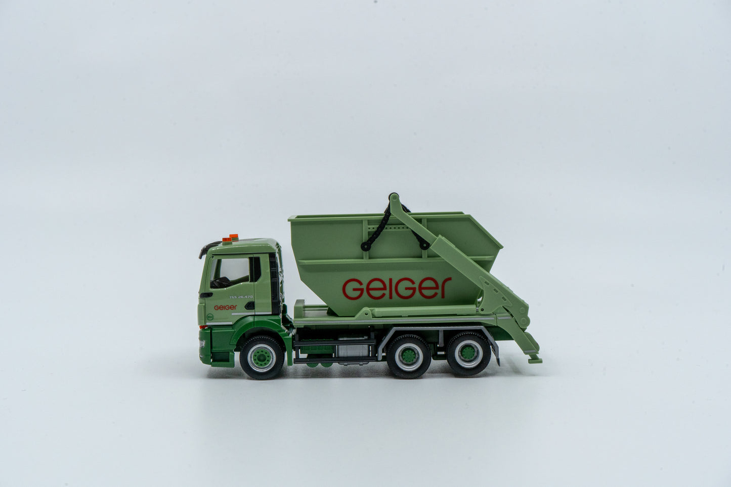 Miniaturmodell eines MAN Geiger-Containerservice-Fahrzeugs in Geiger-Grün mit rotem "Geiger" Schriftzug. Verpackung inklusive.