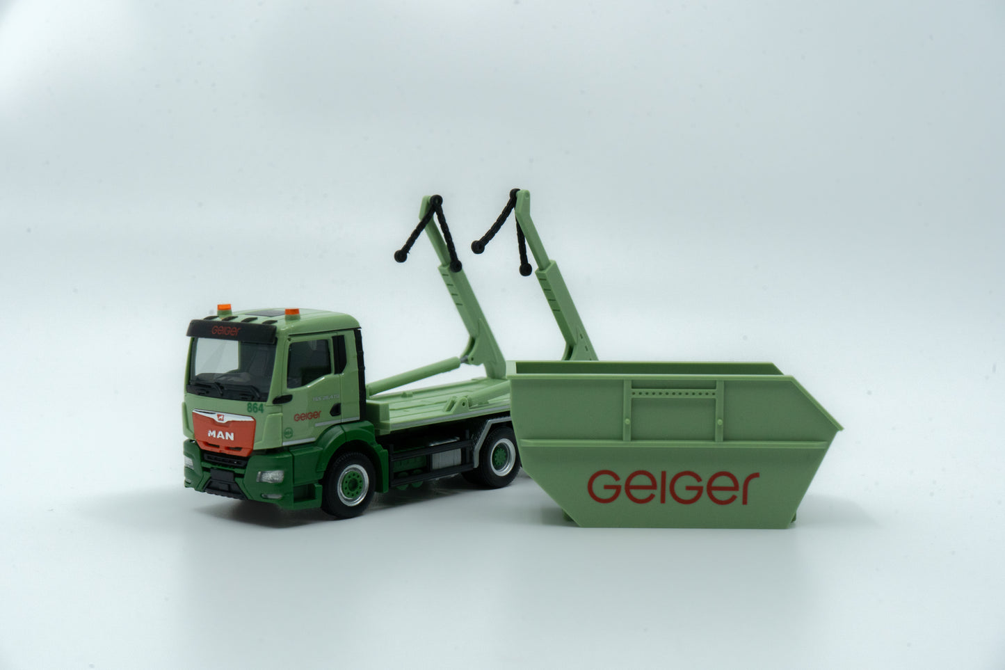 Miniaturmodell eines MAN Geiger-Containerservice-Fahrzeugs in Geiger-Grün mit rotem "Geiger" Schriftzug. Verpackung inklusive.