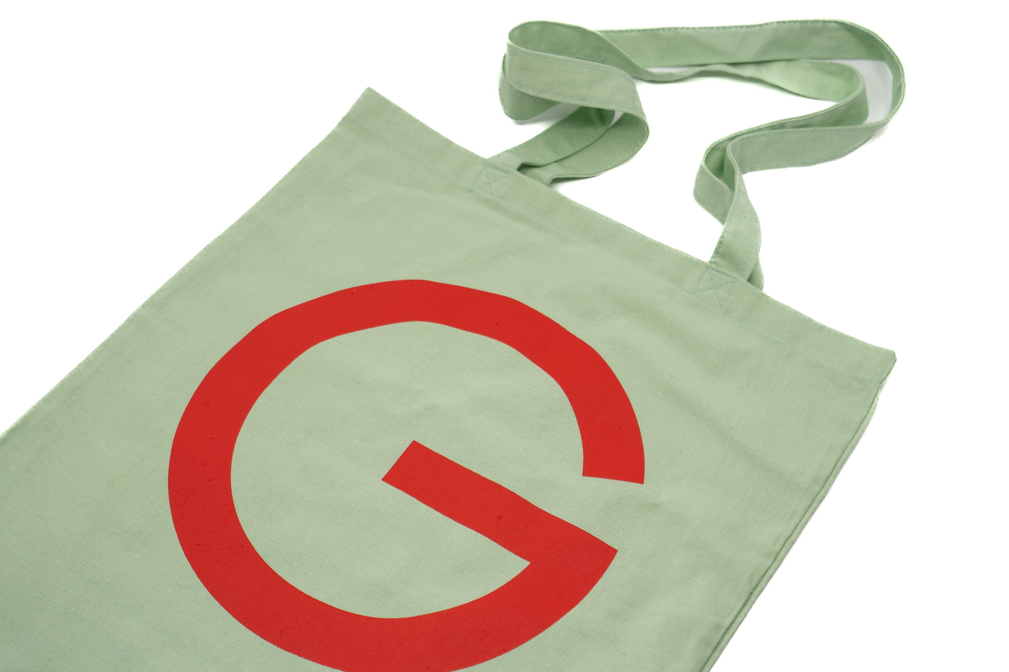 Stofftasche in Geiger-Grün mit einem großen roten „G“ auf der Vorder- und Rückseite und zwei Tragehenkeln.