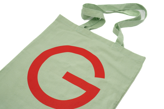 Stofftasche in Geiger-Grün mit einem großen roten „G“ auf der Vorder- und Rückseite und zwei Tragehenkeln.
