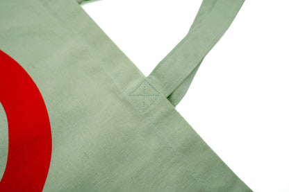 Stofftasche in Geiger-Grün mit einem großen roten „G“ auf der Vorder- und Rückseite und zwei Tragehenkeln.