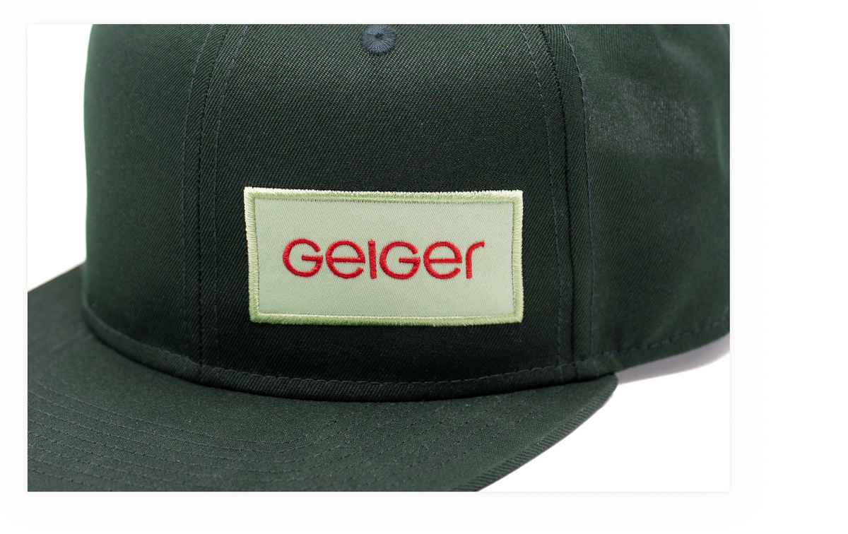 Dunkelgrüne Cap mit flachem Schirm und aufgesticktem Geiger-Logo auf der Vorderseite.