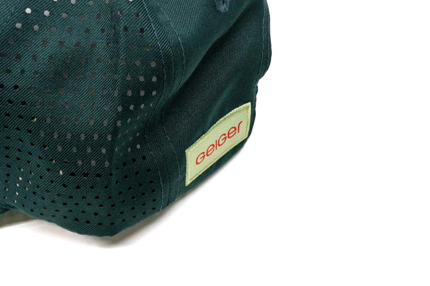 Kiefergrüne Kappe mit gebogenem Schild. Rotes "G" auf Geiger-grünem Hintergrund auf der Vorderseite. Seitlich komplett mit Lüftungslöscher versehen. Rückseite hat ein "Geiger"Logo Patch.