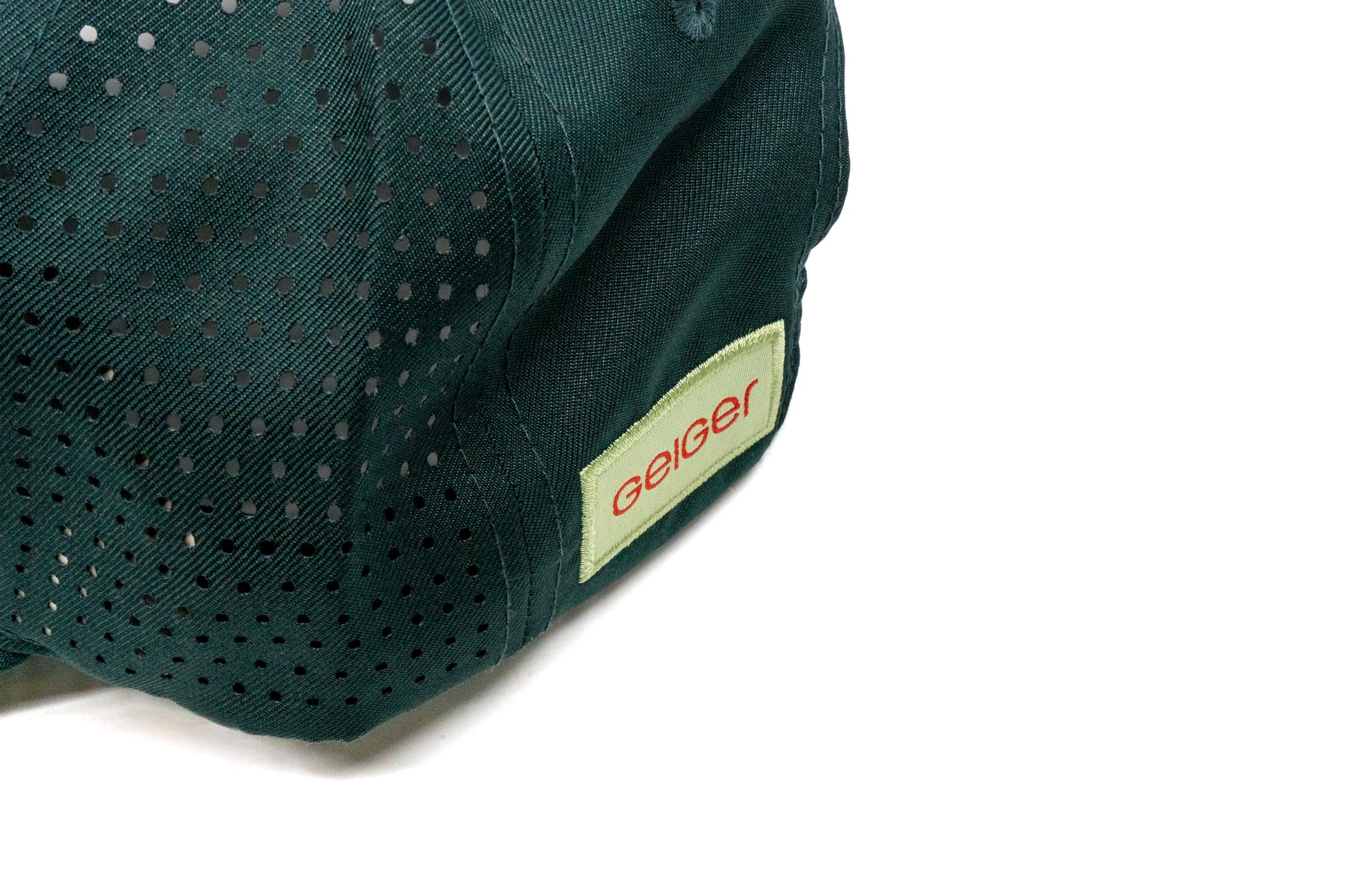 Kiefergrüne Kappe mit gebogenem Schild. Rotes "G" auf Geiger-grünem Hintergrund auf der Vorderseite. Seitlich komplett mit Lüftungslöscher versehen. Rückseite hat ein "Geiger"Logo Patch.