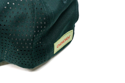 Kiefergrüne Kappe mit gebogenem Schild. Rotes "G" auf Geiger-grünem Hintergrund auf der Vorderseite. Seitlich komplett mit Lüftungslöscher versehen. Rückseite hat ein "Geiger"Logo Patch.