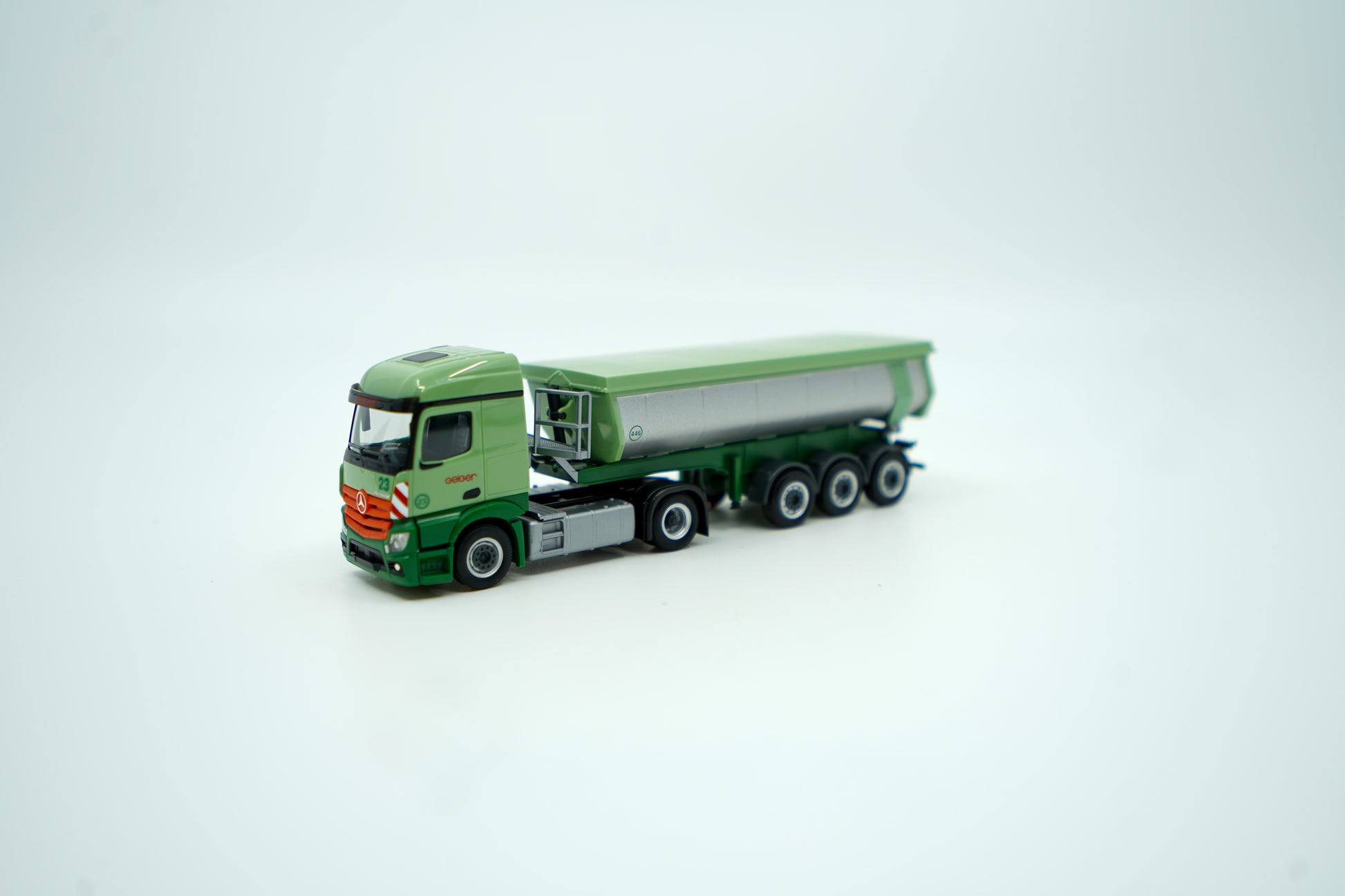 Miniaturmodell eines Mercedes Geiger-LKW in Geiger-Grün mit grauem Thermomulden Anhänger mit rotem "Geiger" Schriftzug. Verpackung inklusive.