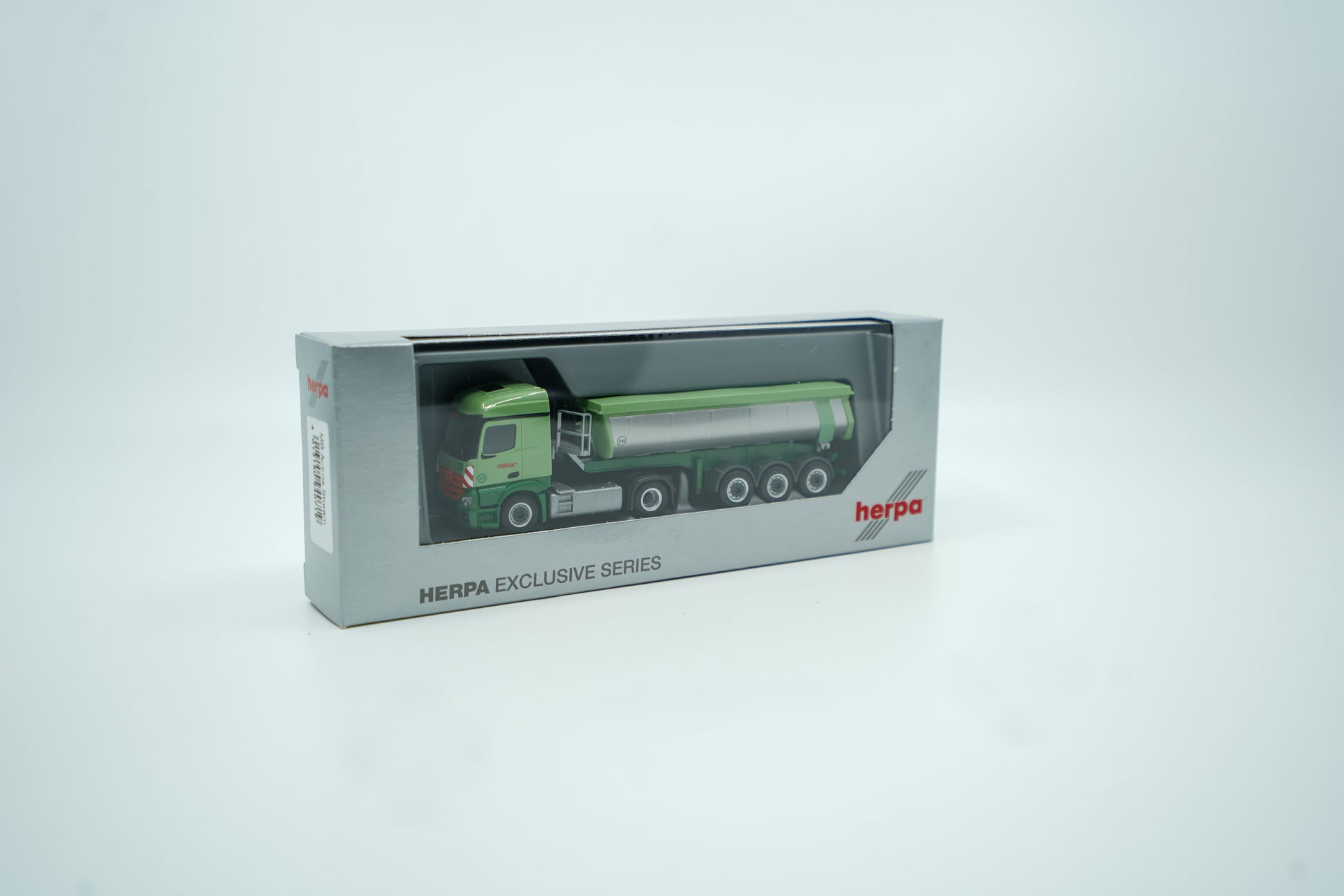 Miniaturmodell eines Mercedes Geiger-LKW in Geiger-Grün mit grauem Thermomulden Anhänger mit rotem "Geiger" Schriftzug. Verpackung inklusive.
