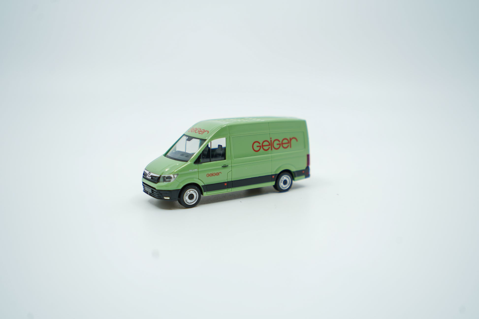 Miniaturmodell eines Geiger MAN-Transporters / Halbbus in Geiger-Grün mit rotem „Geiger“-Schriftzug, Verpackung inklusive.