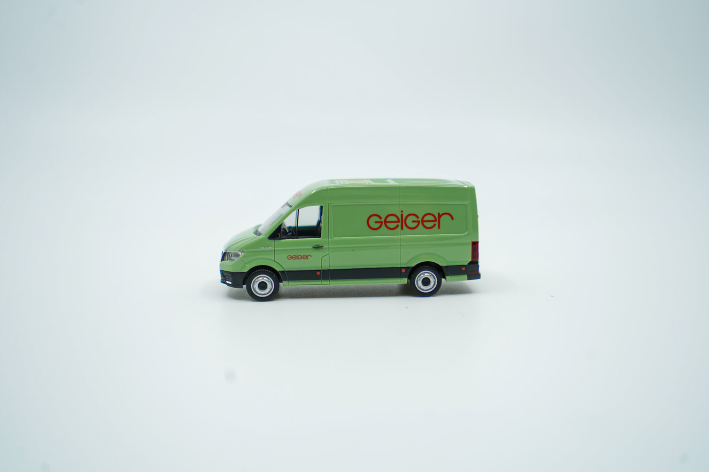 Miniaturmodell eines Geiger MAN-Transporters / Halbbus in Geiger-Grün mit rotem „Geiger“-Schriftzug, Verpackung inklusive.