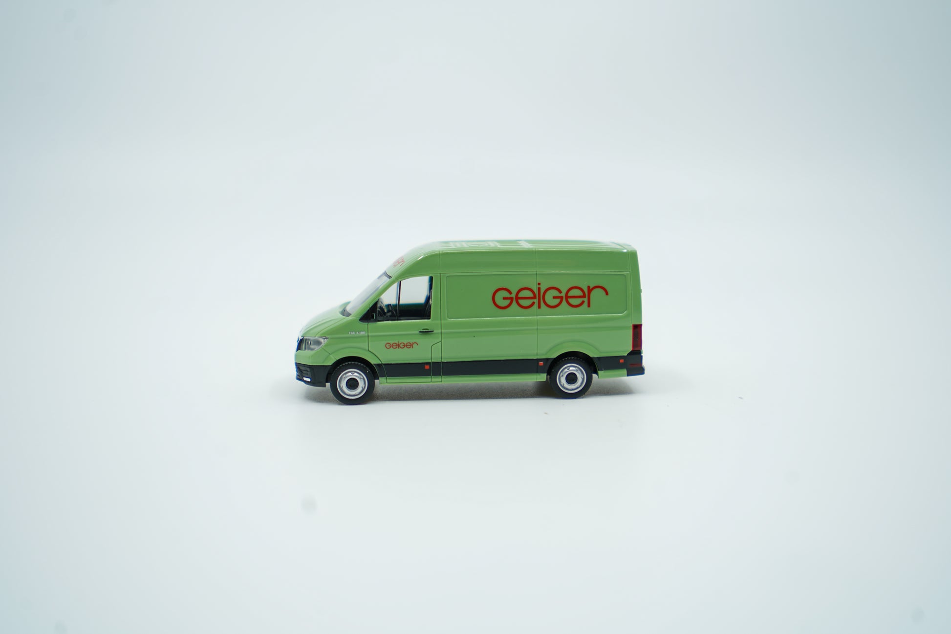 Miniaturmodell eines Geiger MAN-Transporters / Halbbus in Geiger-Grün mit rotem „Geiger“-Schriftzug, Verpackung inklusive.