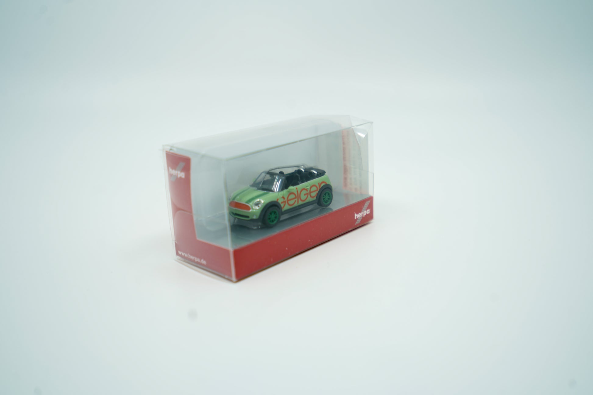 Miniaturmodell eines Geiger Mini-Cooper PKW in Geiger-Grün mit rotem „Geiger“-Schriftzug, Verpackung inklusive.
