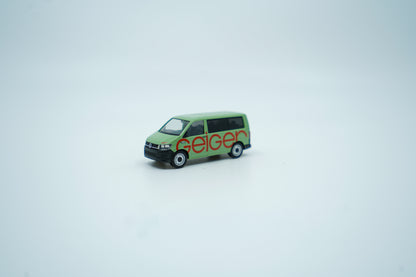 Miniaturmodell eines Geiger VW-Bus in Geiger-Grün mit rotem „Geiger“-Schriftzug, Verpackung inklusive.
