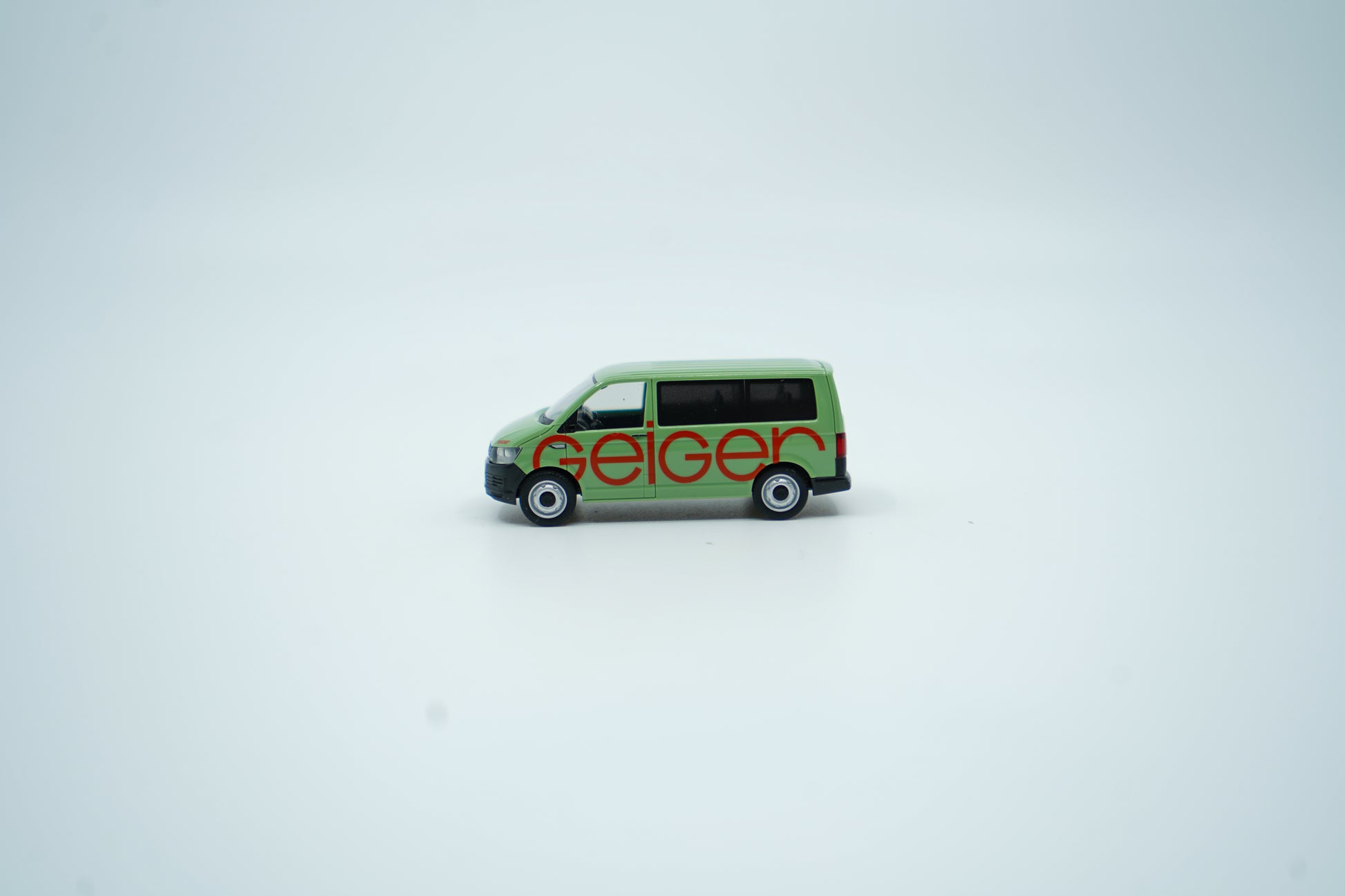Miniaturmodell eines Geiger VW-Bus in Geiger-Grün mit rotem „Geiger“-Schriftzug, Verpackung inklusive.