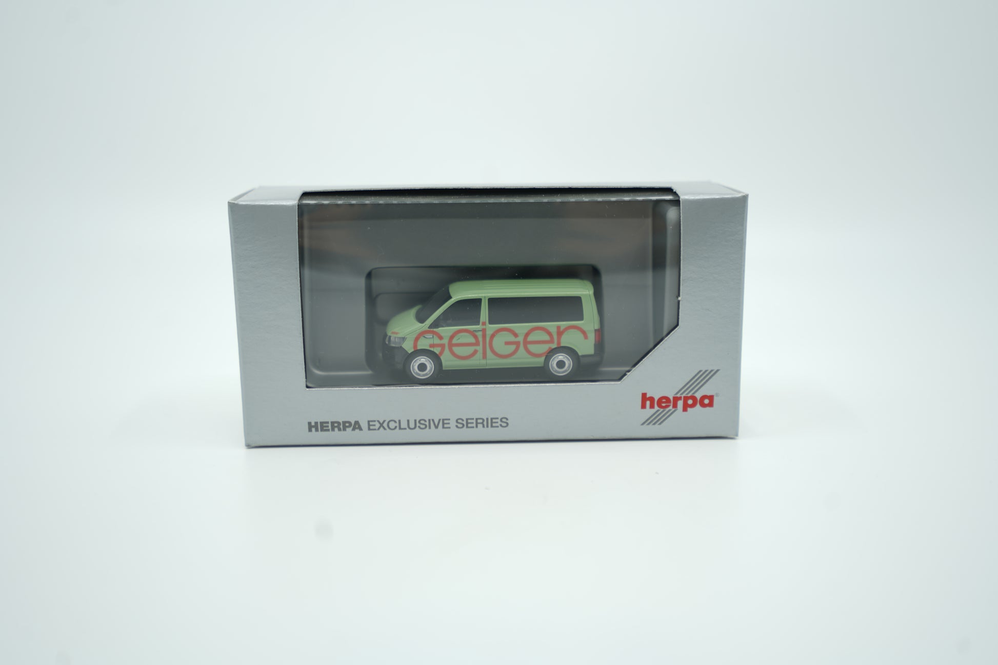 Miniaturmodell eines Geiger VW-Bus in Geiger-Grün mit rotem „Geiger“-Schriftzug, Verpackung inklusive.