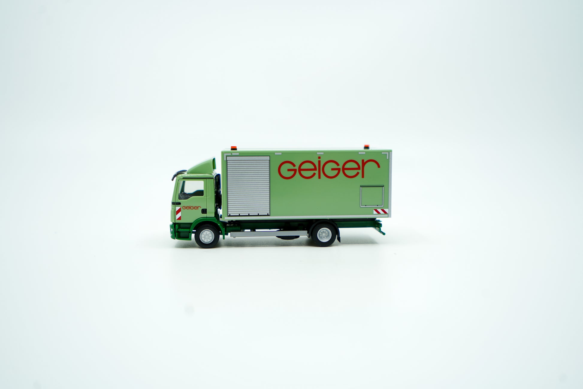 Miniaturmodell eines MAN Geiger-LKW mit geschlossenem Kastenaufbau in Geiger-Grün und rotem "Geiger" Schriftzug. Verpackung inklusive.