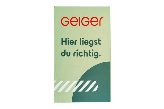 Geiger Grünes Mikrofaserhandtuch mit dem Schriftzug "Hier liegst du richtig." und Geiger Logo.