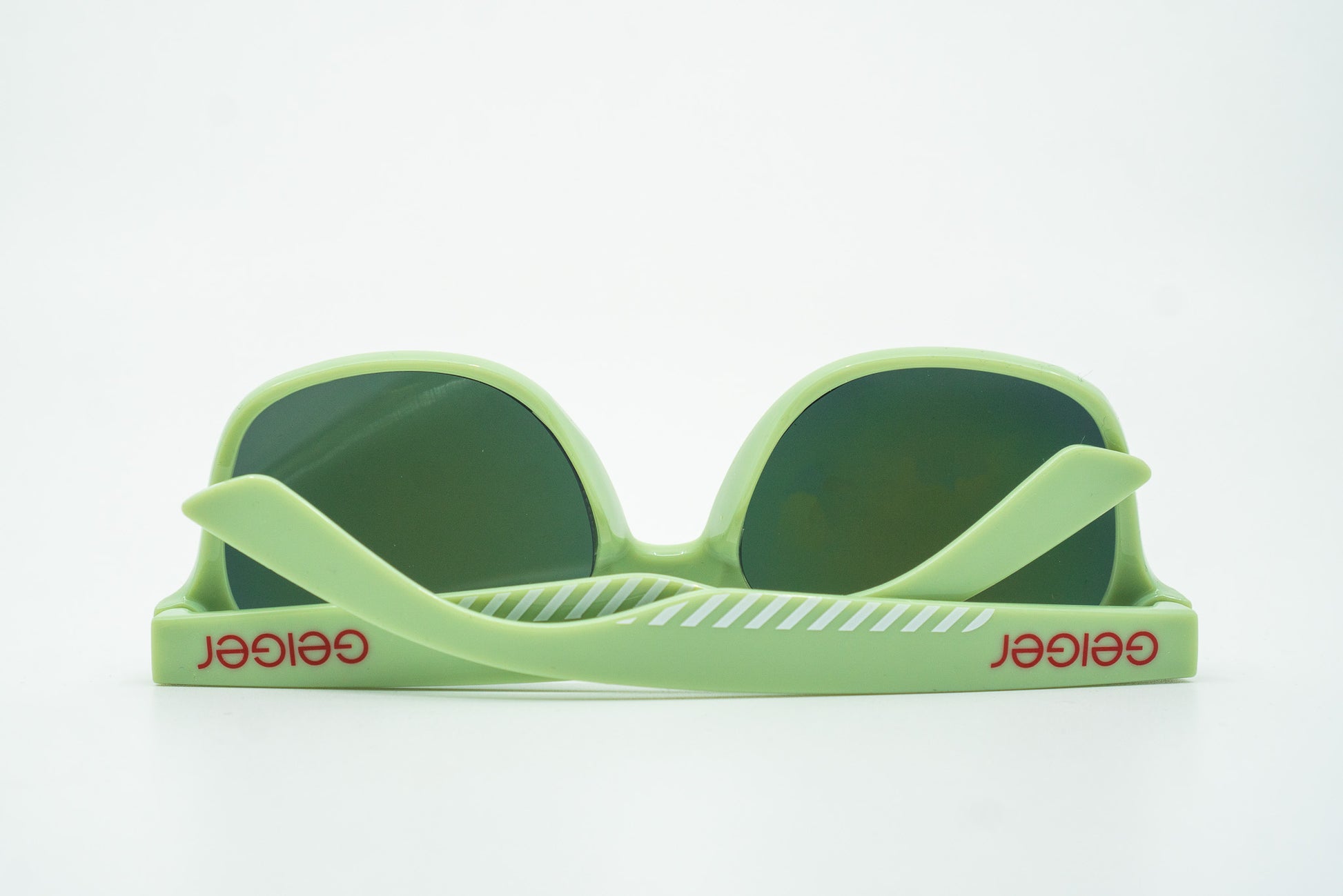 Sonnenbrille in Geiger-Grün mit roten „Geiger“-Schriftzügen an den Bügeln und verspiegelten Gläsern.
